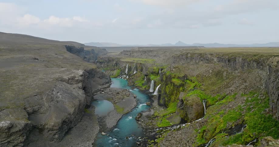 Drone shot flies over a couple hiking to reveal the majestic Sigoldugljufur canyon, with its many waterfalls and turquoise river in Iceland