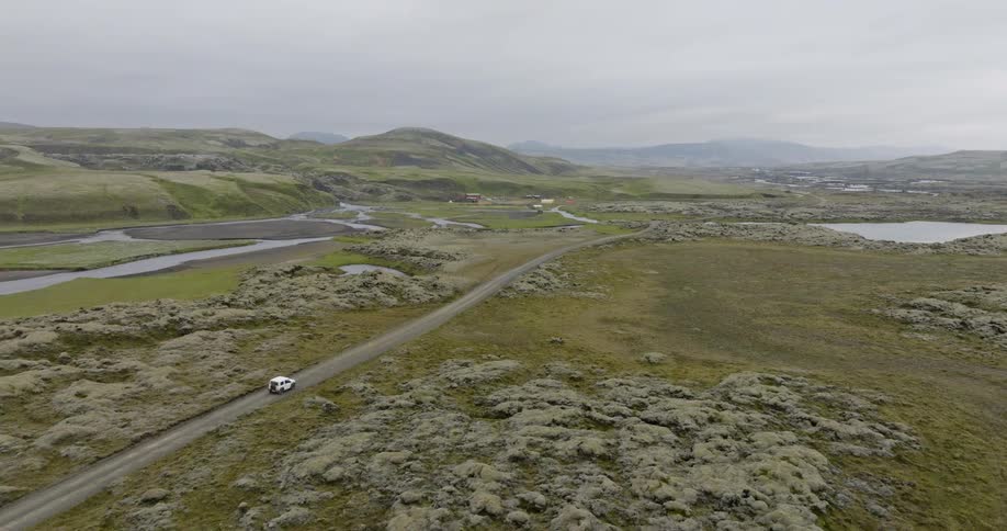 Aerial view of a white camper van on an adventurous road trip through the remote, mossy lava fields of Iceland
