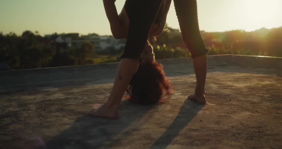 A woman in silhouette dances freely and expressively on a rooftop during a golden sunset in slow motion