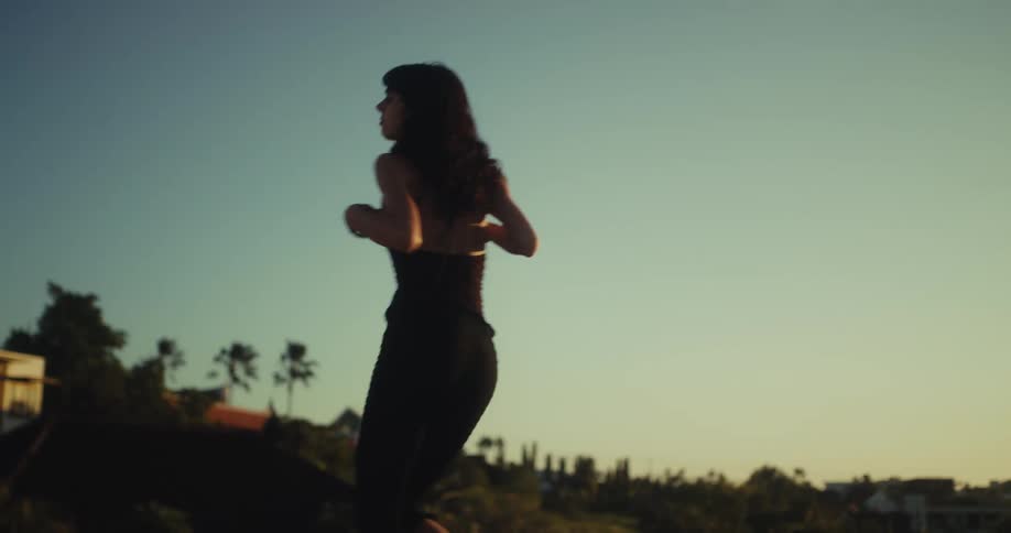 A graceful woman dances barefoot on a rooftop at sunset