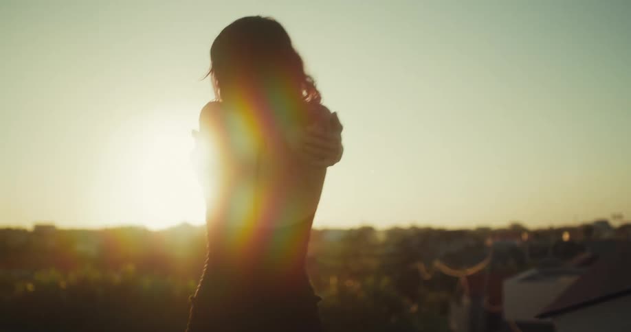 A woman's silhouette dances gracefully in slow motion on a rooftop, her form backlit by the warm glow of the setting sun