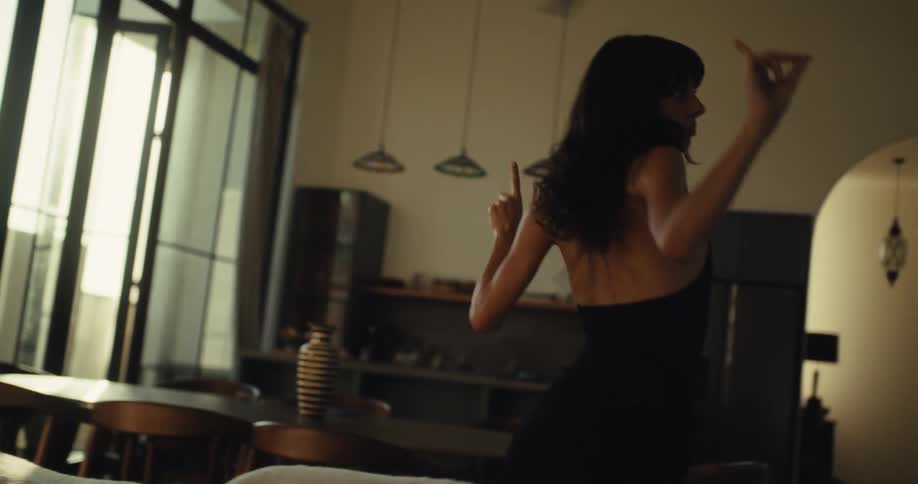 An expressive woman dances with carefree joy in her sunlit modern home in slow motion