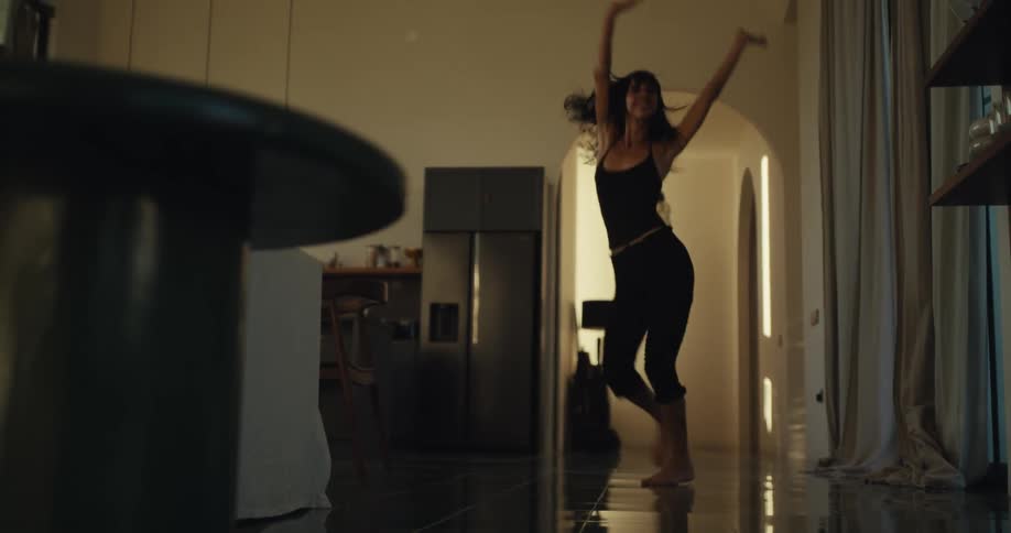 An energetic woman joyfully dances barefoot through the hallway of her modern home in slow motion