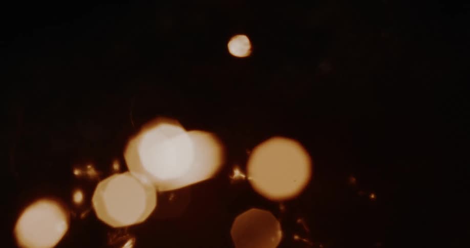 Warm, out-of-focus bokeh lights and glowing sparks dance across a dark, moody background