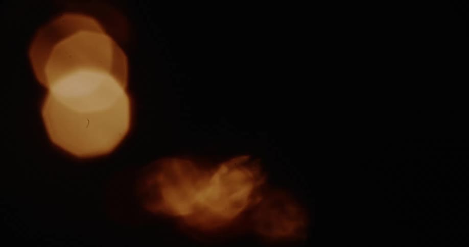 Abstract warm glowing bokeh light orbs float and dance in slow motion against a dark background