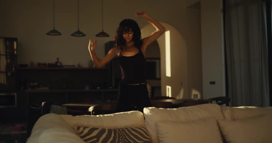 A carefree woman dances with wild abandon in her stylish, sun-drenched living room in slow motion