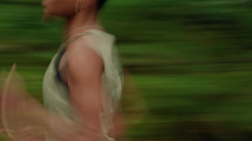 Dynamic motion blur side view of a fit woman running with determination through a lush green environment