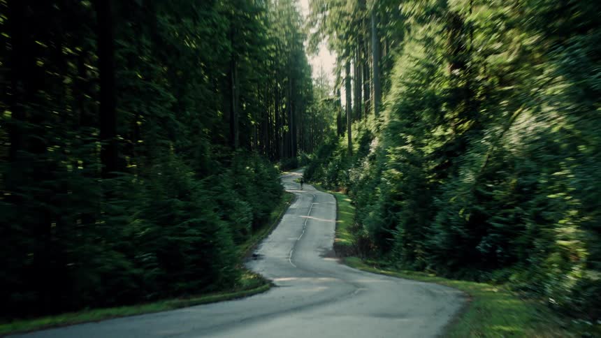 A man runs alone down a winding road through a lush, green forest as the camera dramatically pulls away