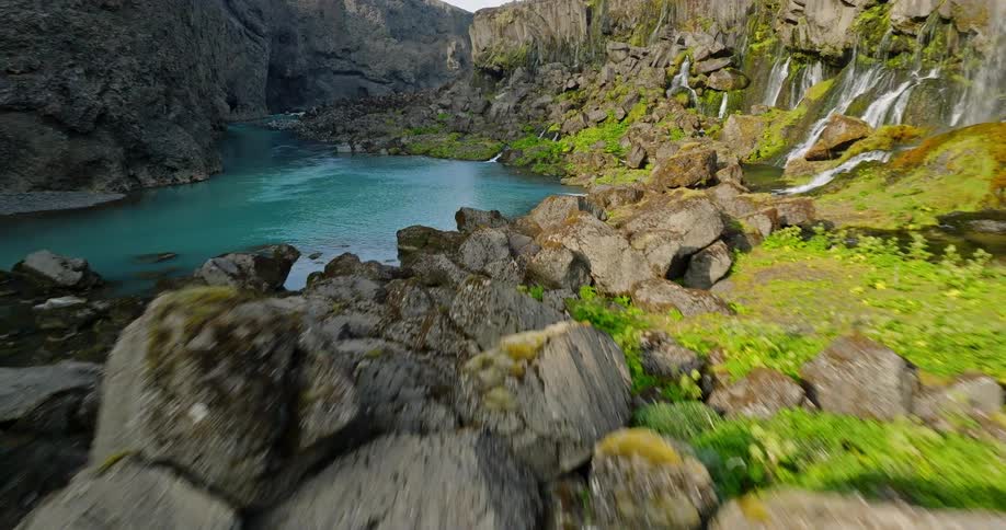A stunning aerial view follows a vibrant turquoise river as it carves through a dramatic rocky canyon with cascading waterfalls