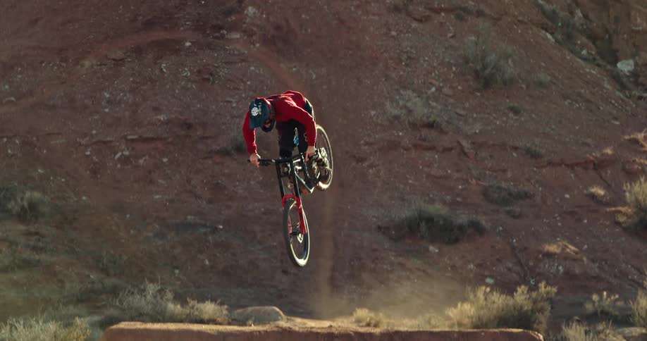 A mountain biker performs an incredibly stylish 360 table trick off a large dirt jump in the desert in slow motion