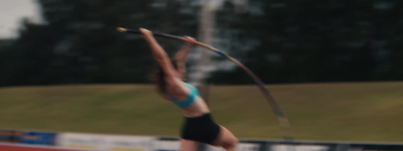 Slow motion side view of a determined female athlete running and successfully completing a pole vault