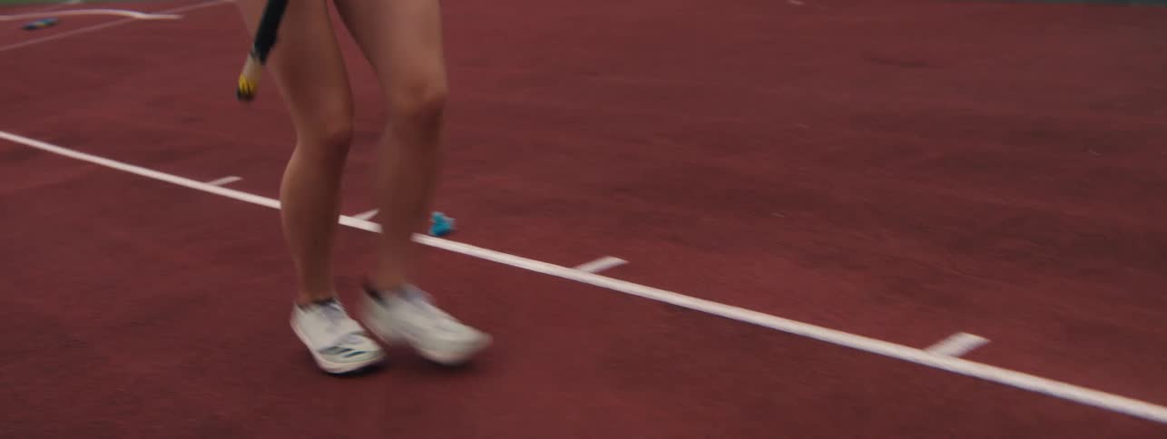 Close-up of a female runner's legs sprinting on a track during a relay race practice, passing a small rubber duck