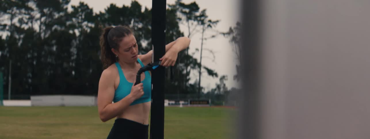 A focused female athlete adjusts her resistance training equipment on a track and field before a workout