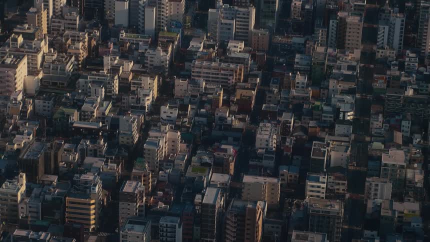 A high-angle static shot shows a dense urban cityscape with buildings illuminated by the warm light of sunset