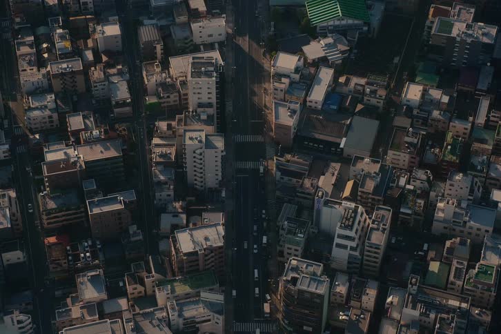 A static top-down aerial shot captures light traffic moving through a dense urban city during the warm light of golden hour