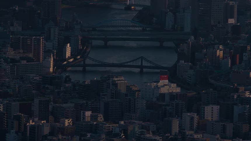 A static aerial view captures the moody atmosphere of a dense city with its river and bridges as dusk settles