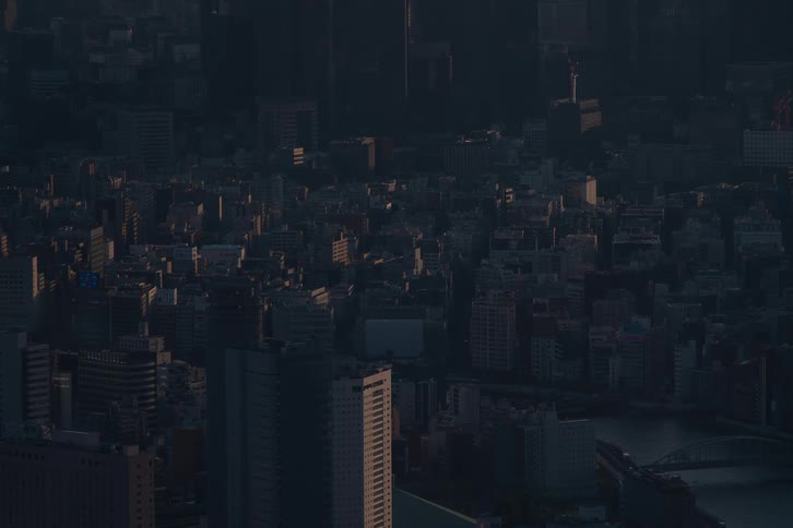 An aerial view of a sprawling metropolitan city as the sun slowly begins to rise, gradually illuminating the dark buildings