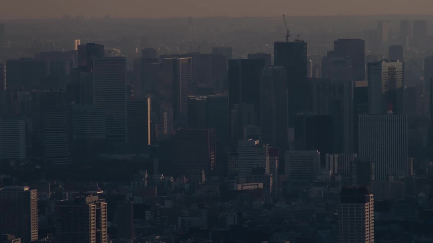Golden hour light illuminates the hazy skyline of a vast, modern city