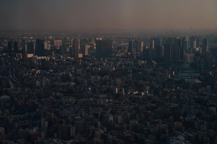 A wide, static aerial shot captures the immense urban sprawl of a major city at dusk, with buildings stretching to the hazy horizon