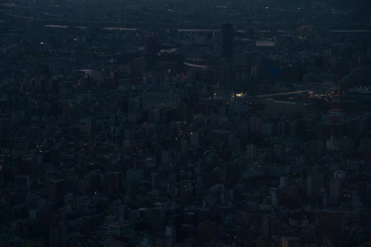 Wide aerial view of a sprawling metropolis at twilight as the city's lights begin to twinkle in the darkness