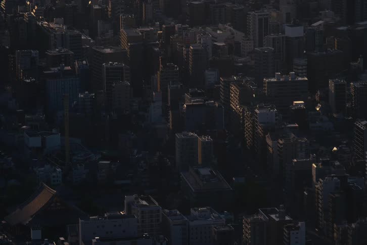A single beam of sunrise light sweeps across the shadowed buildings of a dense urban city
