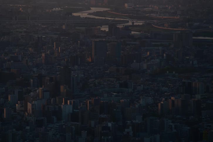 Static high angle view of a vast cityscape with a river and highways bathed in the dim light of dusk