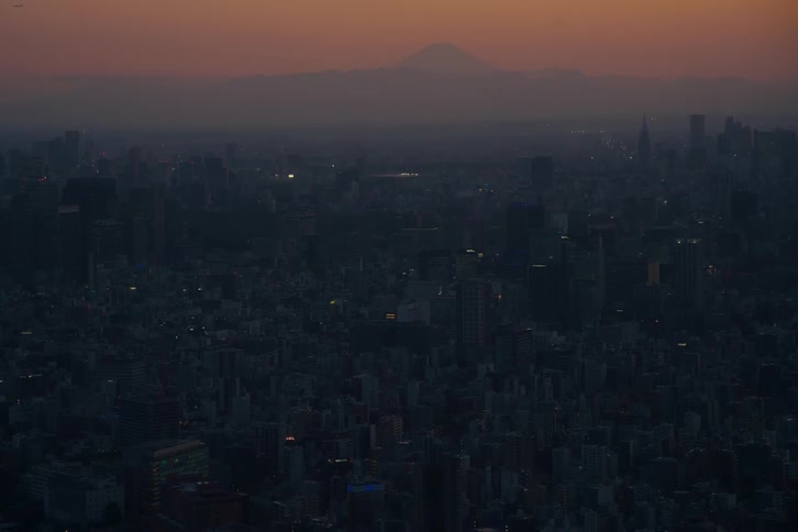 A serene aerial view of the vast Tokyo cityscape at dusk with the iconic silhouette of Mount Fuji visible on the horizon