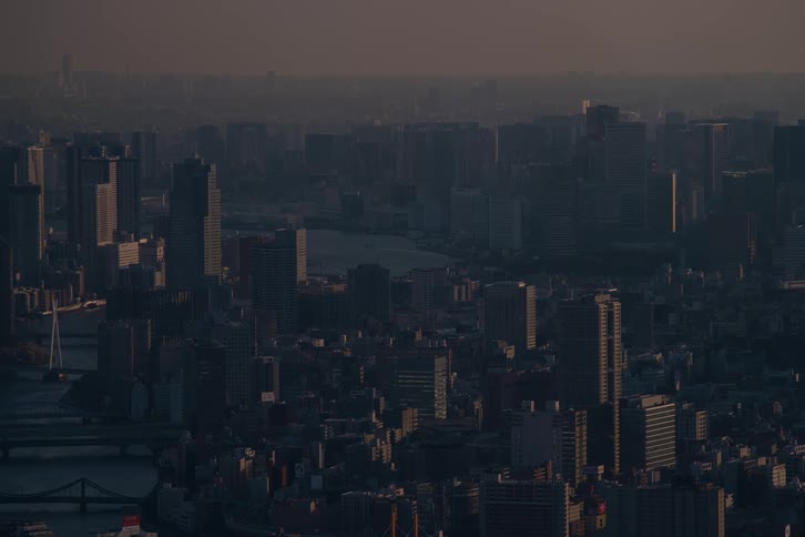 A vast and hazy cityscape of a major metropolis bathed in the warm, muted light of sunrise or sunset