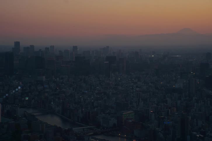 An expansive aerial shot captures the twilight descending over Tokyo, with the iconic Mount Fuji silhouetted against the colorful sky