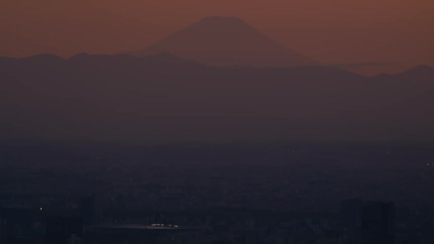 Mount Fuji stands majestically over the hazy Tokyo cityscape during a warm, tranquil sunset