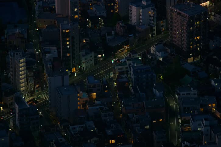 High-angle time-lapse captures streaks of car lights moving through the quiet streets of a dense Tokyo neighborhood at night