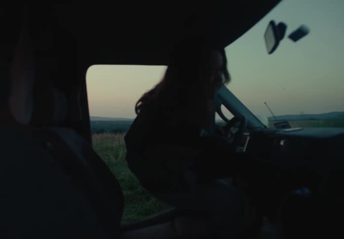 Slow motion shot of a young woman getting into her van in a serene field at dusk