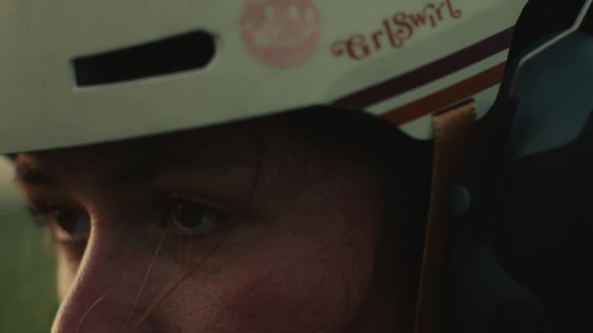A focused female skater with a helmet opens her eyes in a slow-motion close-up during a beautiful sunset