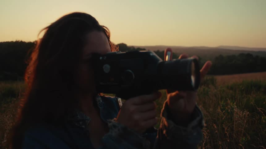 A young woman uses a vintage Super 8 camera to film the scenic landscape during a beautiful golden hour sunset