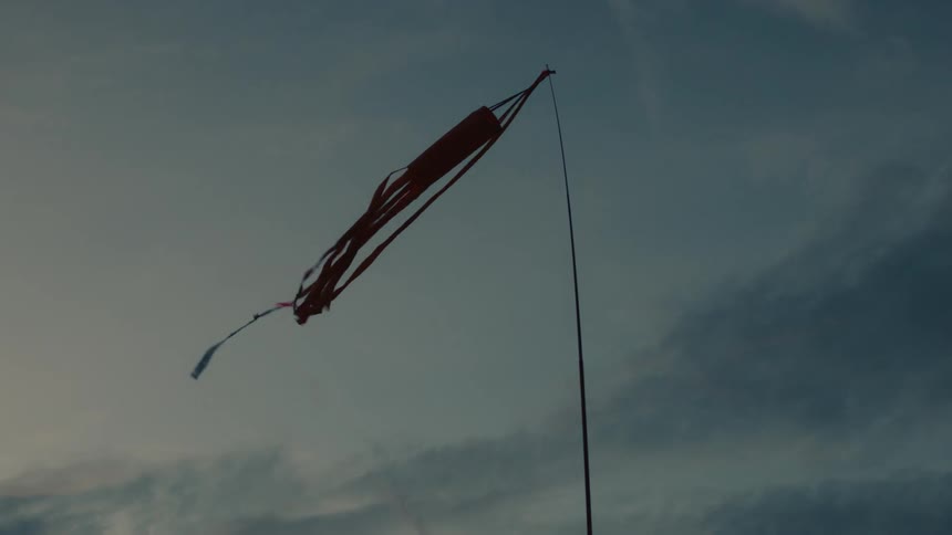 A silhouetted red ribbon kite on a pole gently blows in the wind against a cloudy sky at dusk