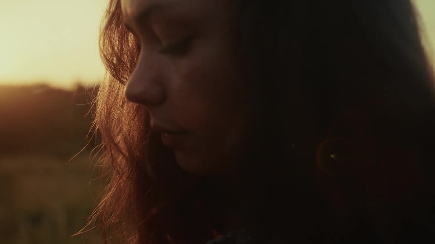 A close-up profile shot of a sad woman crying as a single tear rolls down her cheek in a field at sunset