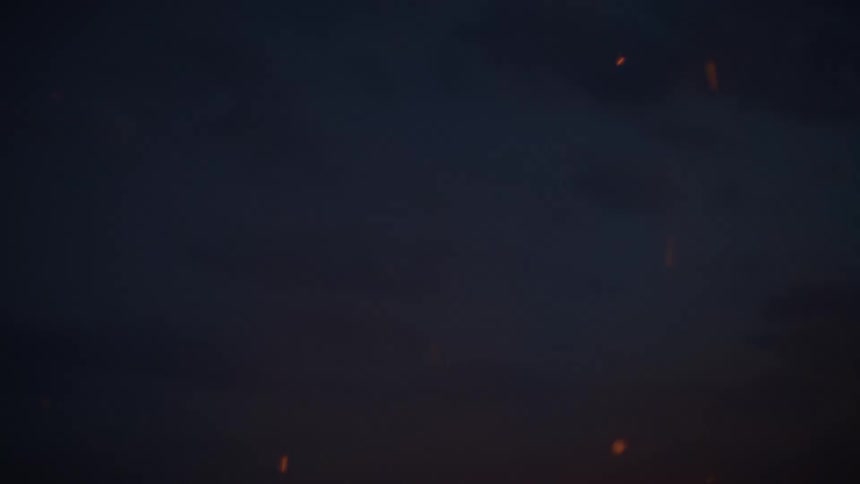 A close-up slow-motion shot of sparks and embers from a bonfire floating up into the dark night sky