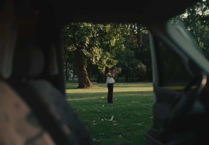 Framed from inside a car, a female photographer captures images in a tranquil park at golden hour