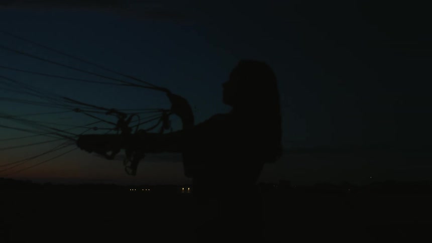A woman's silhouette holds the lines of her paraglider at dusk after the sun has set