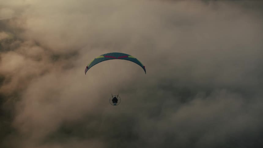 A majestic aerial view of a powered paraglider soaring through a sea of clouds during a golden sunset