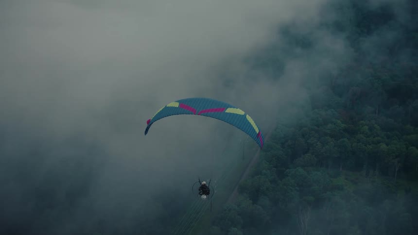Cinemagraph of a paraglider peacefully suspended in the foggy air above a lush mountain landscape