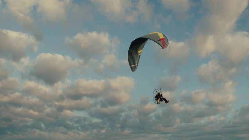 A powered paraglider gracefully soars across a sky filled with beautiful clouds at sunset