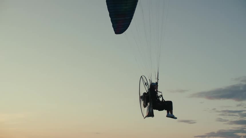 A silhouetted paramotor pilot peacefully hovers in the sky against the beautiful backdrop of a sunset