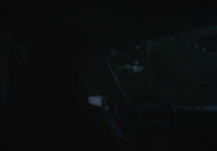 Over-the-shoulder slow pan from the back seat of a person driving a car on a dark road at night