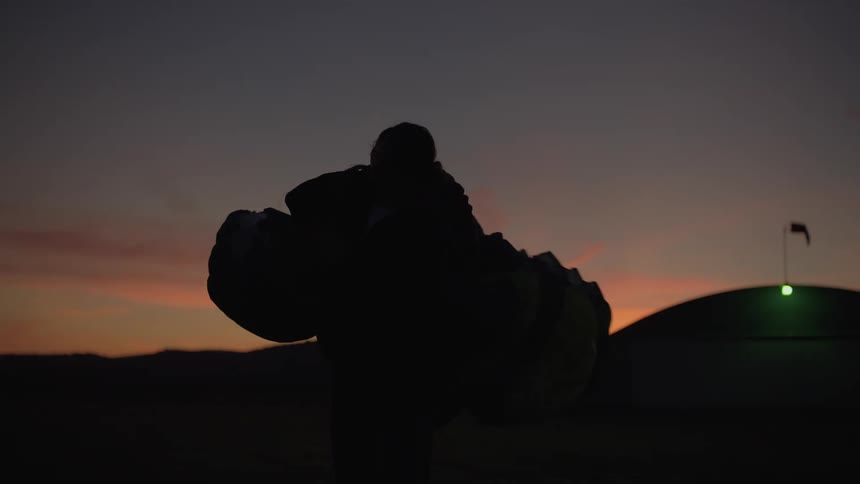 Slow motion silhouette of a female skydiver carefully packing up her parachute after a jump as the sun sets beautifully in the background