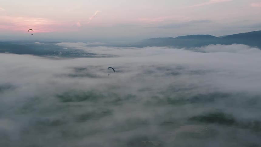 An aerial view of multiple paragliders soaring peacefully above a dense layer of clouds at sunrise