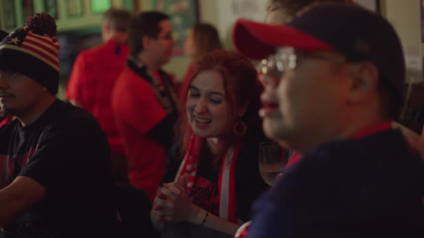Sports fans in a crowded bar anxiously watch a game together, their faces showing a range of emotions