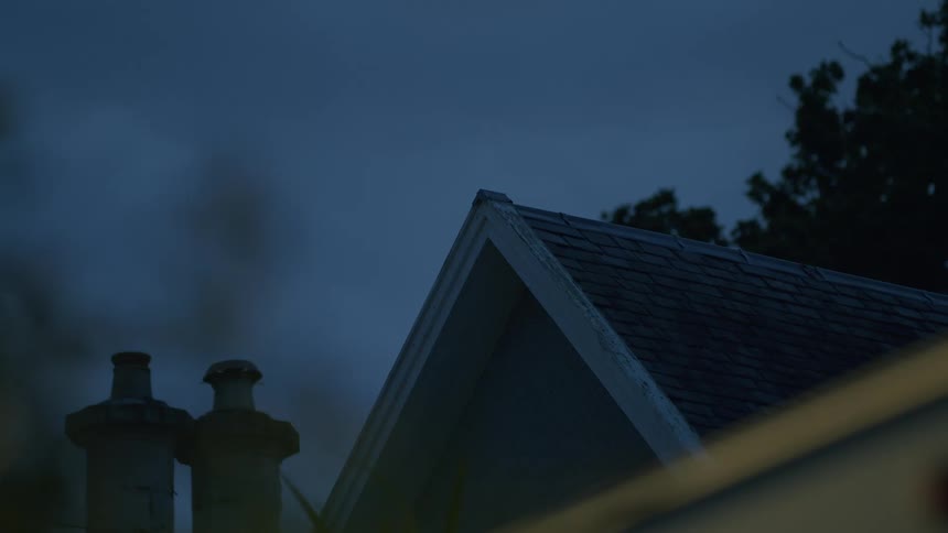 A close up of the top of a house roof on a dark cloudy night