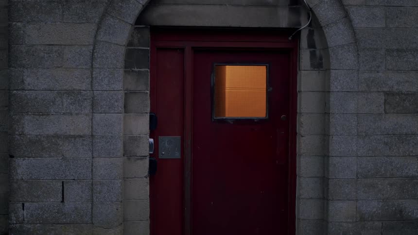 A mysterious red door with a warmly lit window in a stone archway at dusk