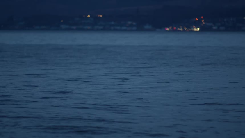 A serene view of a calm blue lake at twilight with distant city lights blurred on the horizon